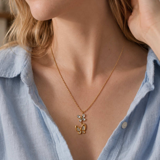 In Motion Butterfly Necklace worn alone with a light blue shirt, showing the double butterfly pendant at the neckline