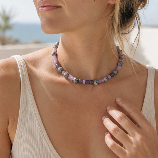 Model wearing a purple and gray natural stone beaded necklace in soft daylight.