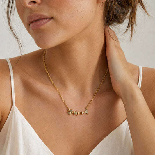 Model wearing a small gold fishbone necklace with subtle zirconia sparkle.
