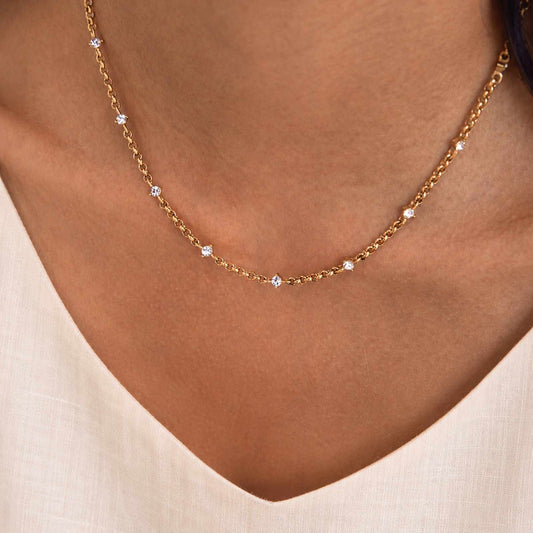 Model wearing a delicate gold zircon chain necklace close to the collarbone.
