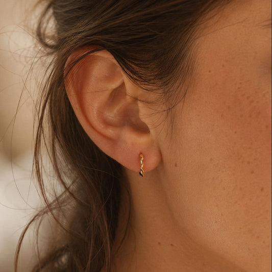Small gold twisted huggie hoop earrings worn on the ear