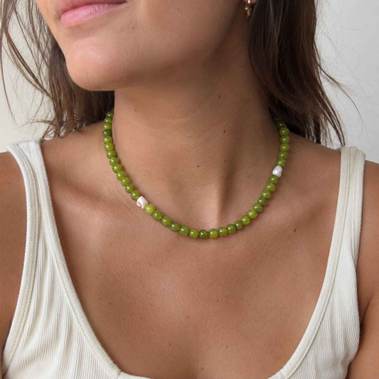 Model wearing an olive green stone necklace with small pearl and shell details.