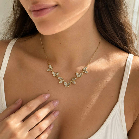 Model wearing a gold butterfly necklace with subtle zircon shine in natural sunlight.
