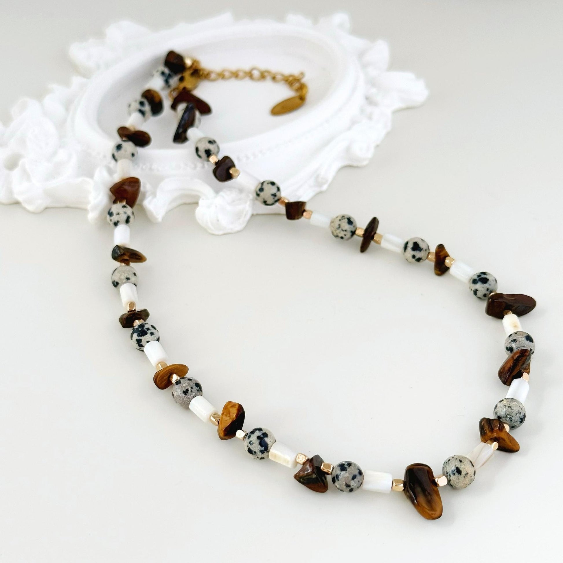 Close-up of tiger eye chips, spotted stone beads, white shell beads, and gold-tone details.