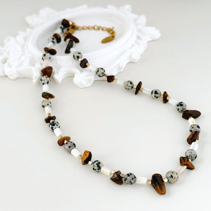 Close-up of tiger eye chips, spotted stone beads, white shell beads, and gold-tone details.