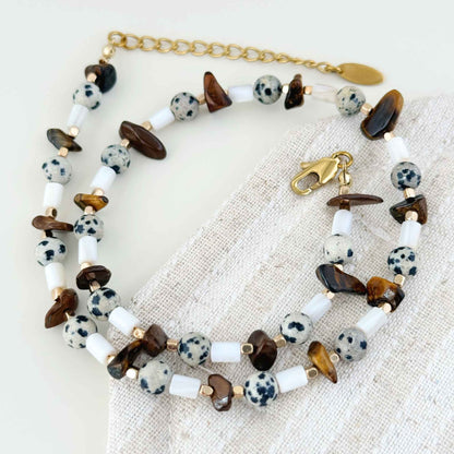 Brown tiger eye and shell necklace arranged on soft linen in natural light.