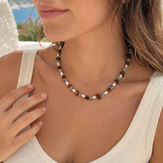 Model wearing a brown tiger eye and shell beaded necklace with a white tank.
