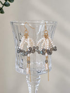 Arc labradorite pearl earrings hanging from a clear glass display, showing their layered structure and long drops.