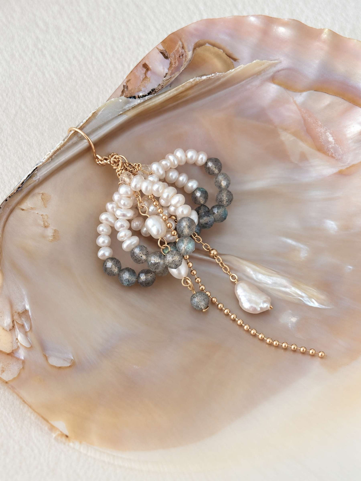Arc freshwater pearl and labradorite earrings styled on a natural shell with warm gold-tone details.