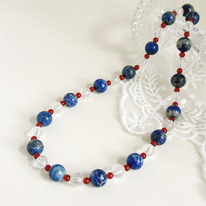Blue and clear natural stone necklace with red accents styled on a clean light surface.
