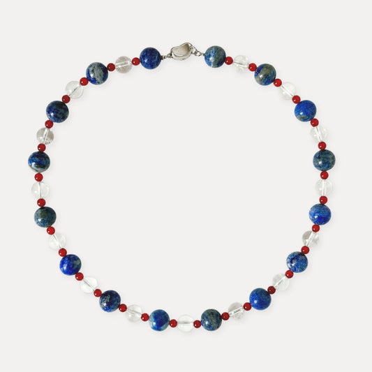 Blue, red, and clear natural stone beaded necklace arranged on a light background.