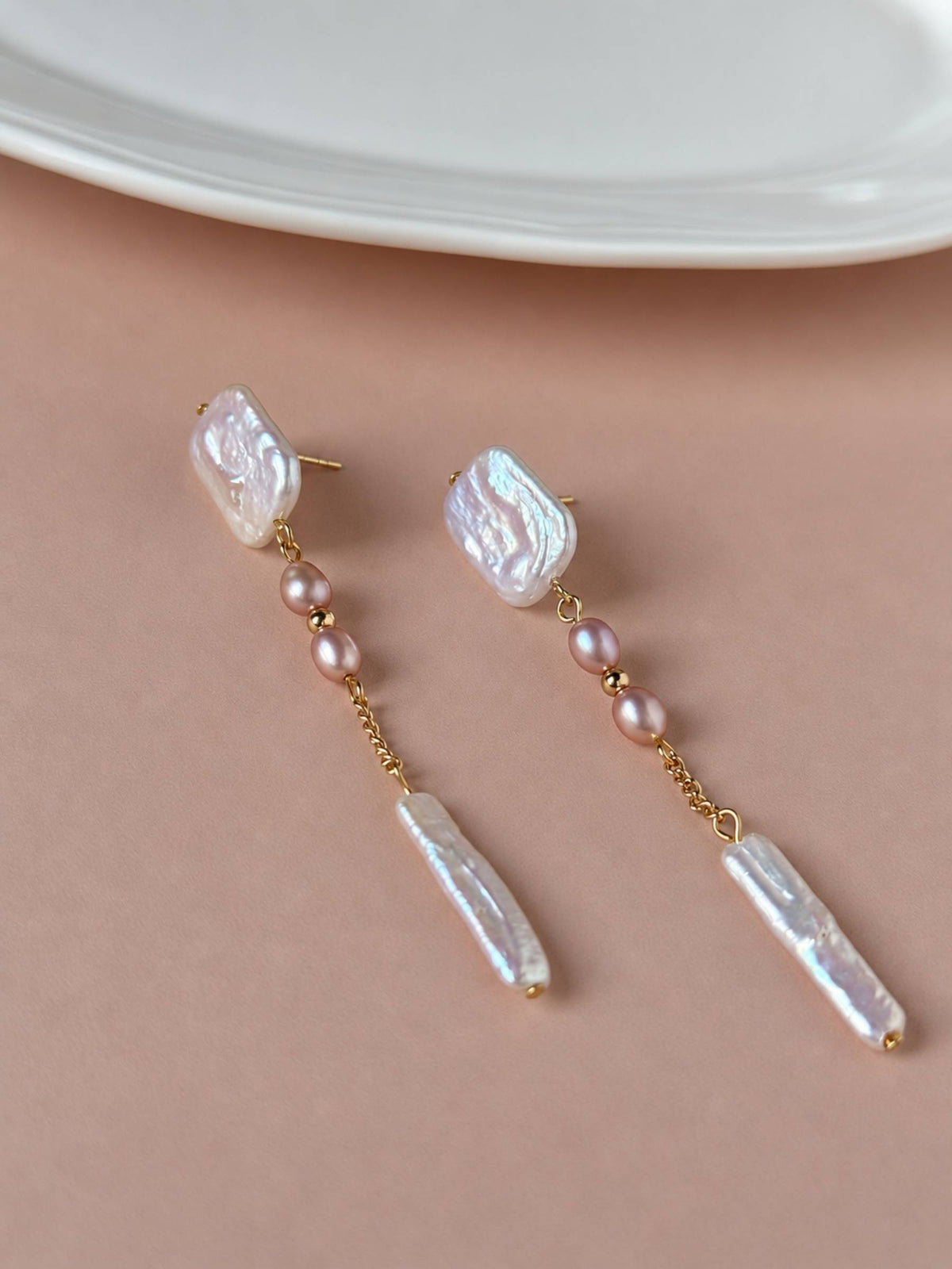 Cadence freshwater pearl drop earrings arranged on a warm neutral surface with pink pearl accents.
