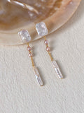 Cadence long freshwater pearl earrings styled beside a natural shell on a textured ivory surface.