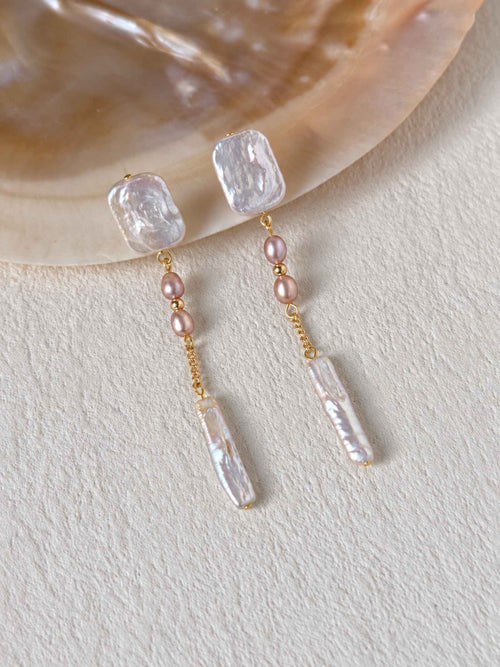 Cadence long freshwater pearl earrings styled beside a natural shell on a textured ivory surface.