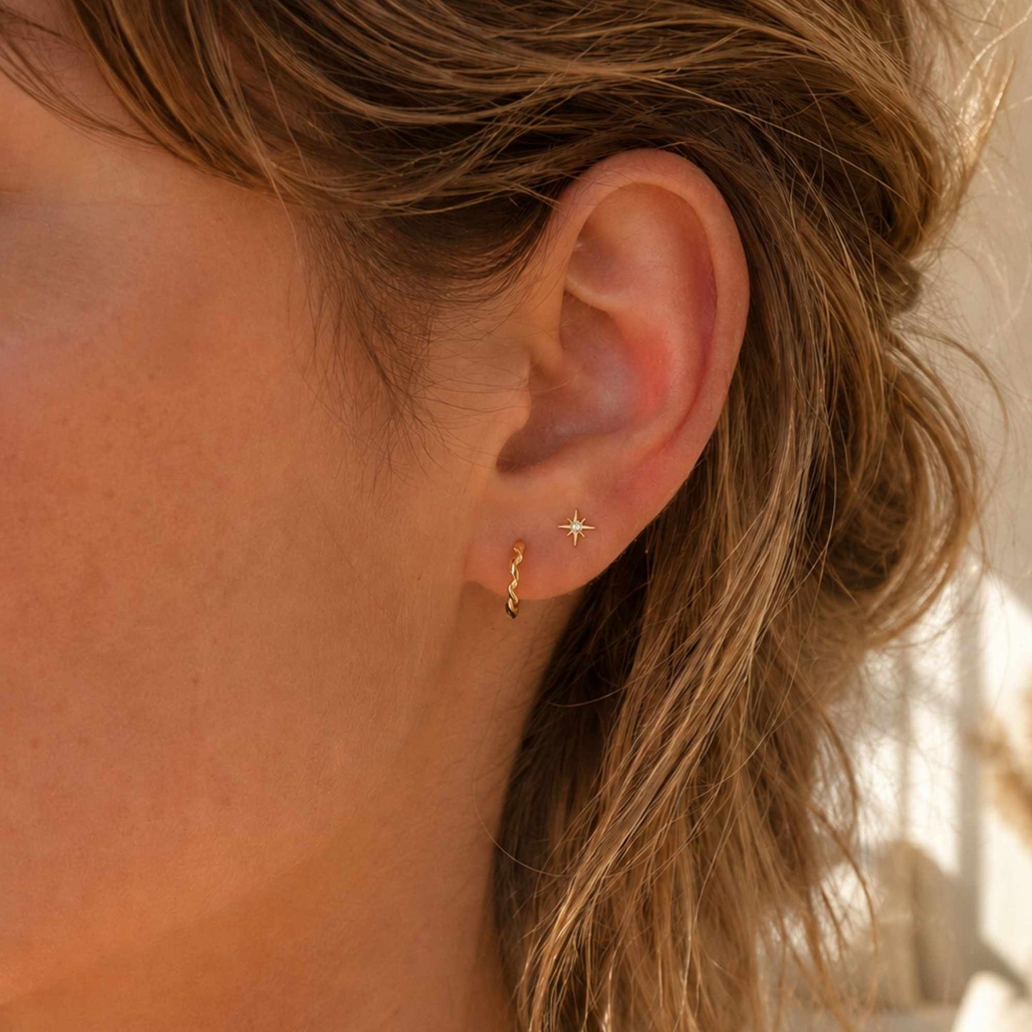 Tiny gold star stud earrings worn on the ear in warm natural light