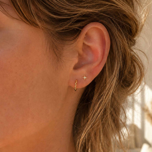 Tiny gold star stud earrings worn on the ear in warm natural light