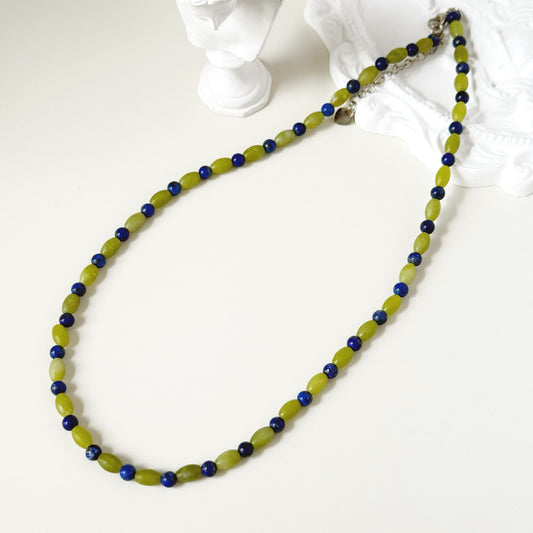 Blue and green beaded necklace styled on a white surface with soft everyday light.