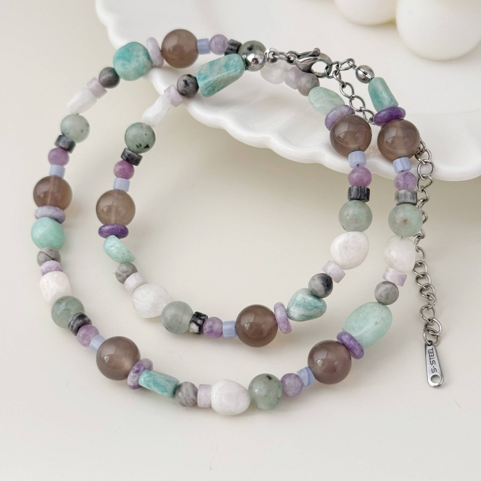 Blue-gray mixed stone necklace arranged on an open book in soft natural light.