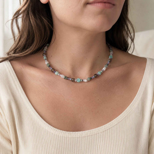 Model wearing a soft blue-gray mixed stone necklace with freshwater pearl accents.