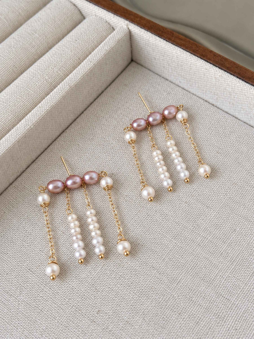 Contour pearl fringe earrings arranged on a linen tray, showing the layered chains and pearl drops.