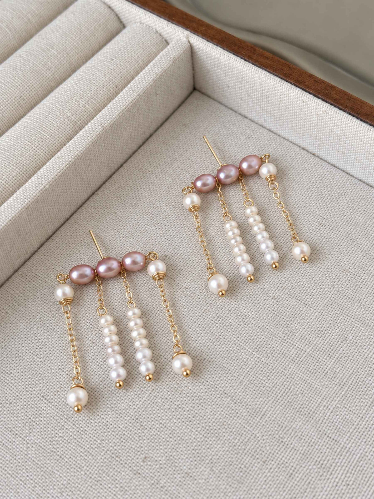 Contour pearl fringe earrings arranged on a linen tray, showing the layered chains and pearl drops.