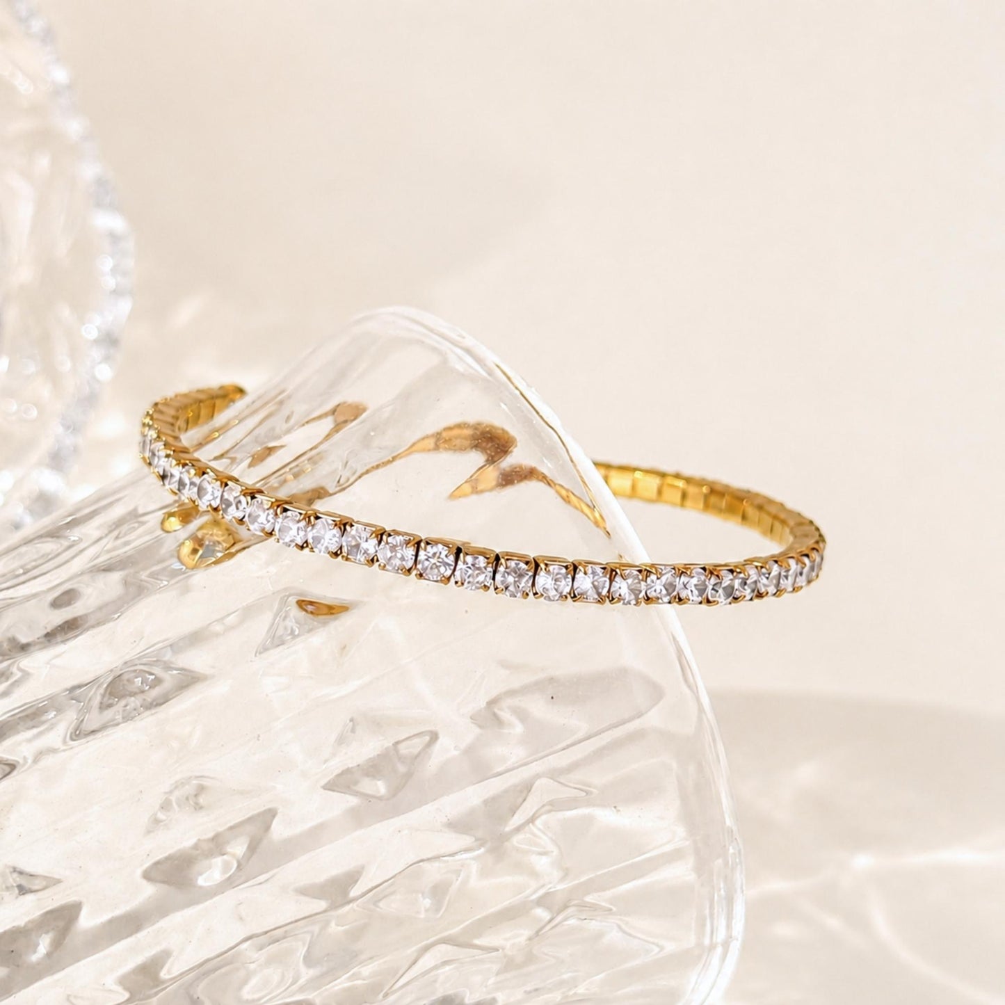 Gold Crossline CZ Bracelet styled across clear textured glass in soft natural light