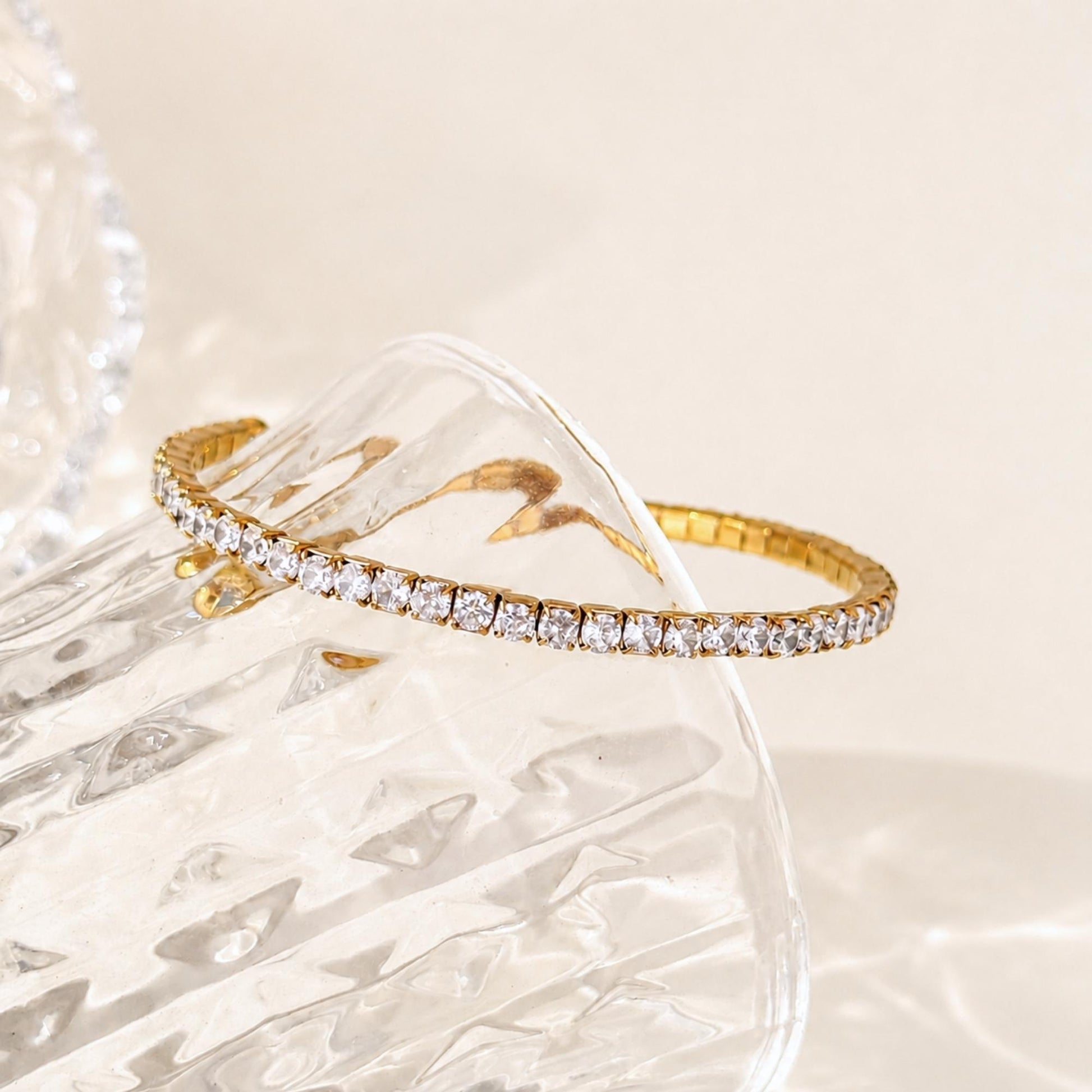 Gold Crossline CZ Bracelet styled across clear textured glass in soft natural light