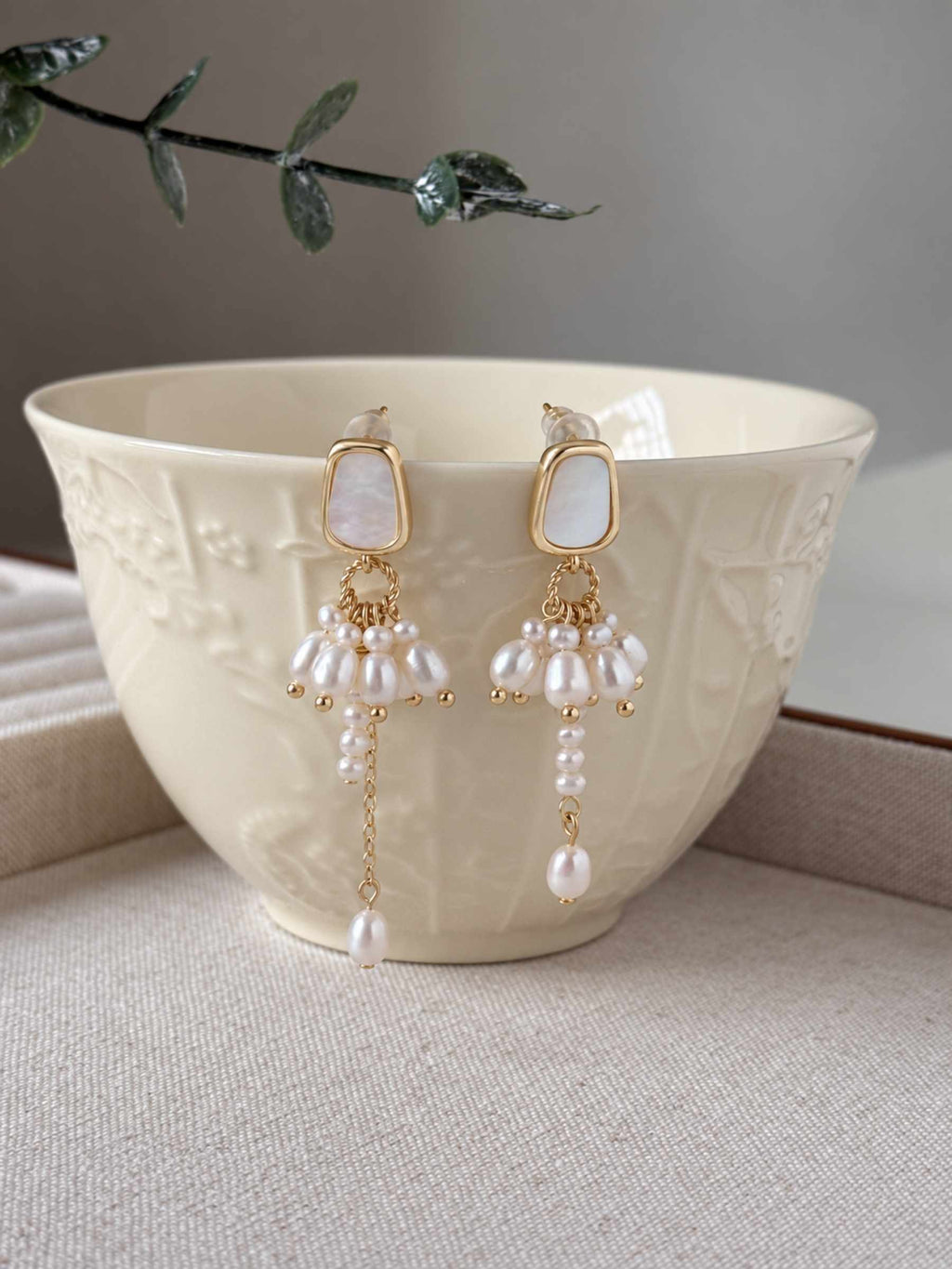 Drape freshwater pearl earrings displayed against a warm ceramic bowl, showing their asymmetric pearl drops.