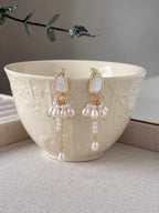 Drape freshwater pearl earrings displayed against a warm ceramic bowl, showing their asymmetric pearl drops.