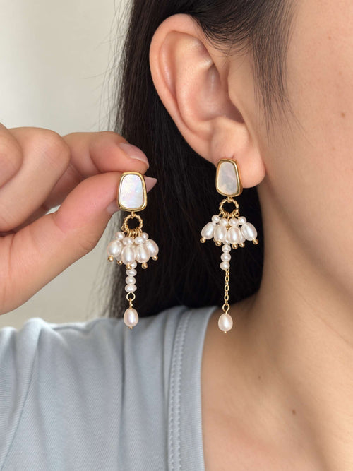 Drape freshwater pearl earrings shown worn and held beside the ear, highlighting their asymmetric lengths.