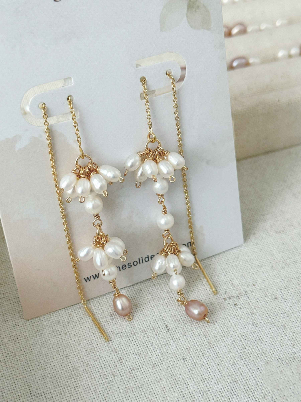 Pair of Drift freshwater pearl threader earrings displayed on a jewelry card, showing the asymmetric clustered drops.