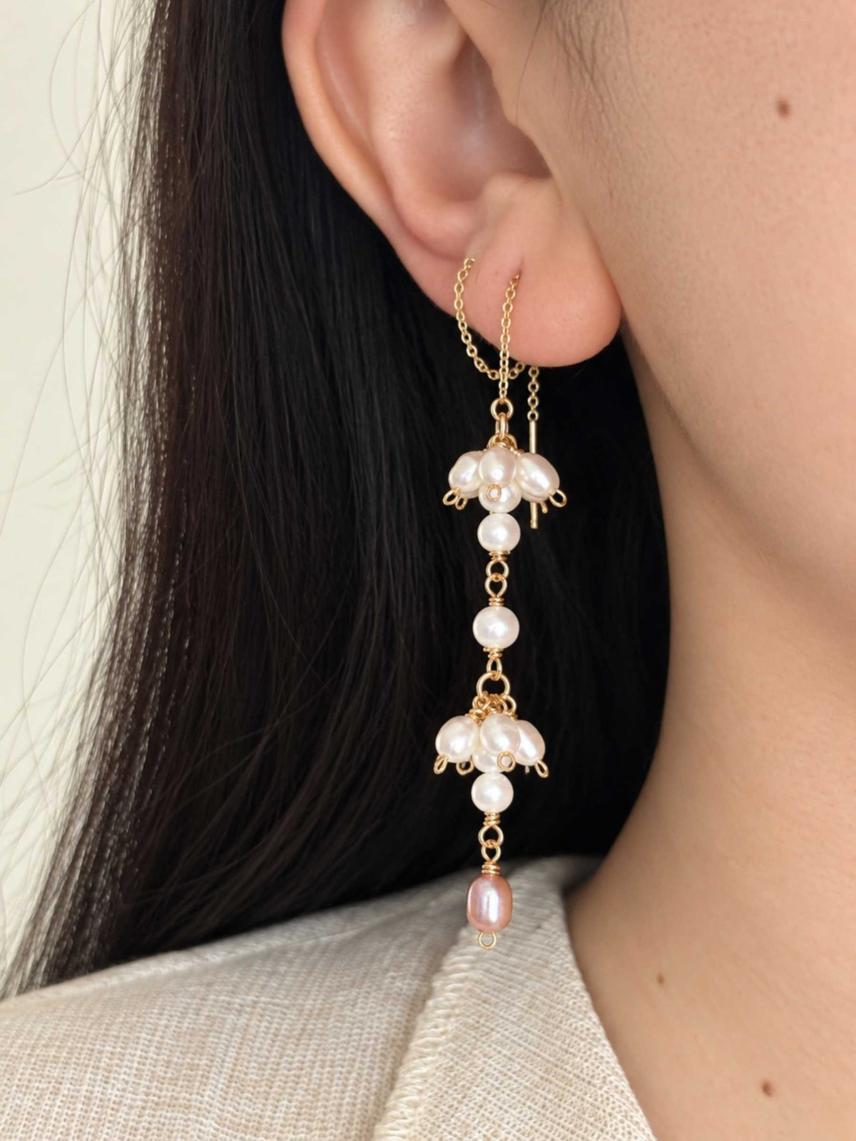 Long Drift pearl threader earring worn through the ear, showing the asymmetric pearl clusters and blush pearl drop.