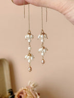 Drift freshwater pearl threader earrings held in the air, showing their long fine chains and asymmetric pearl arrangement.