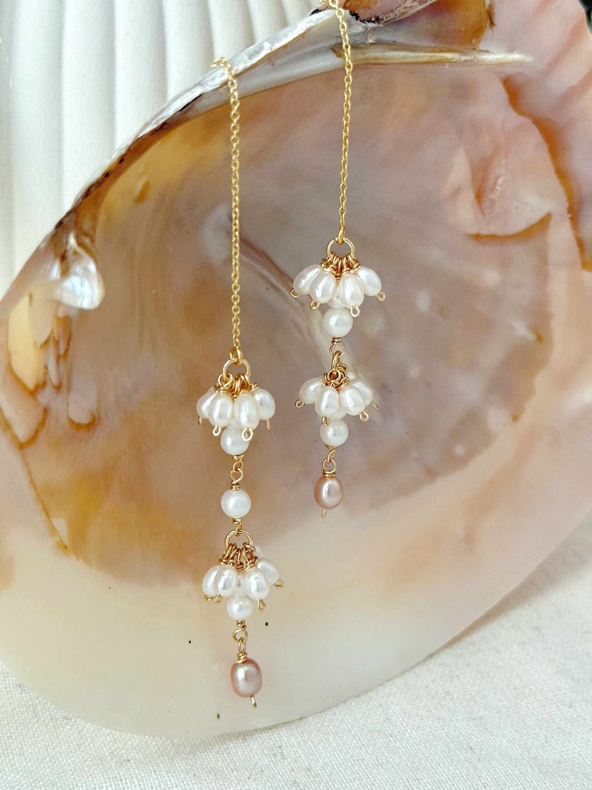 Drift pearl threader earrings suspended against a natural shell background with warm gold and soft pearl tones.