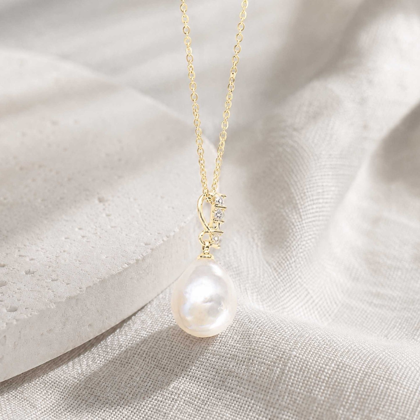 Side detail of natural baroque freshwater pearl pendant with cubic zirconia accents on a soft light-gold chain