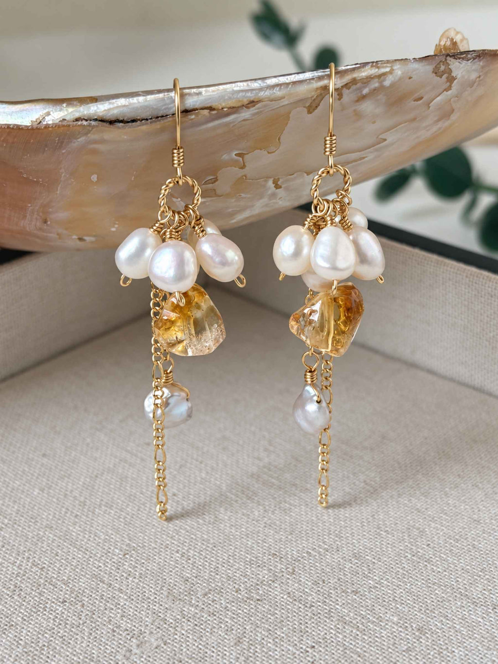 Gleam freshwater pearl and citrine earrings displayed against a natural shell and neutral linen background.