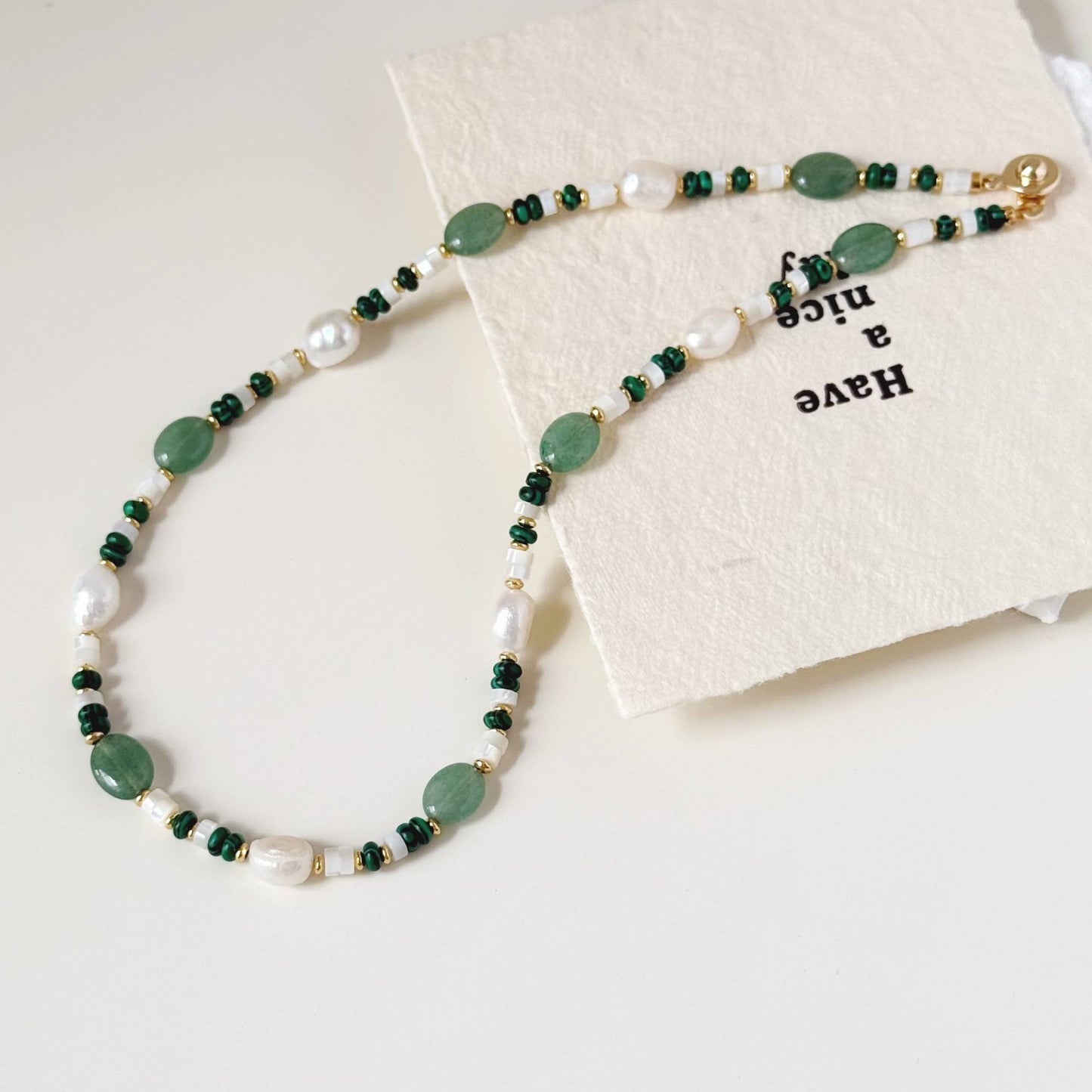 Soft green natural stone and pearl necklace styled on a light surface.