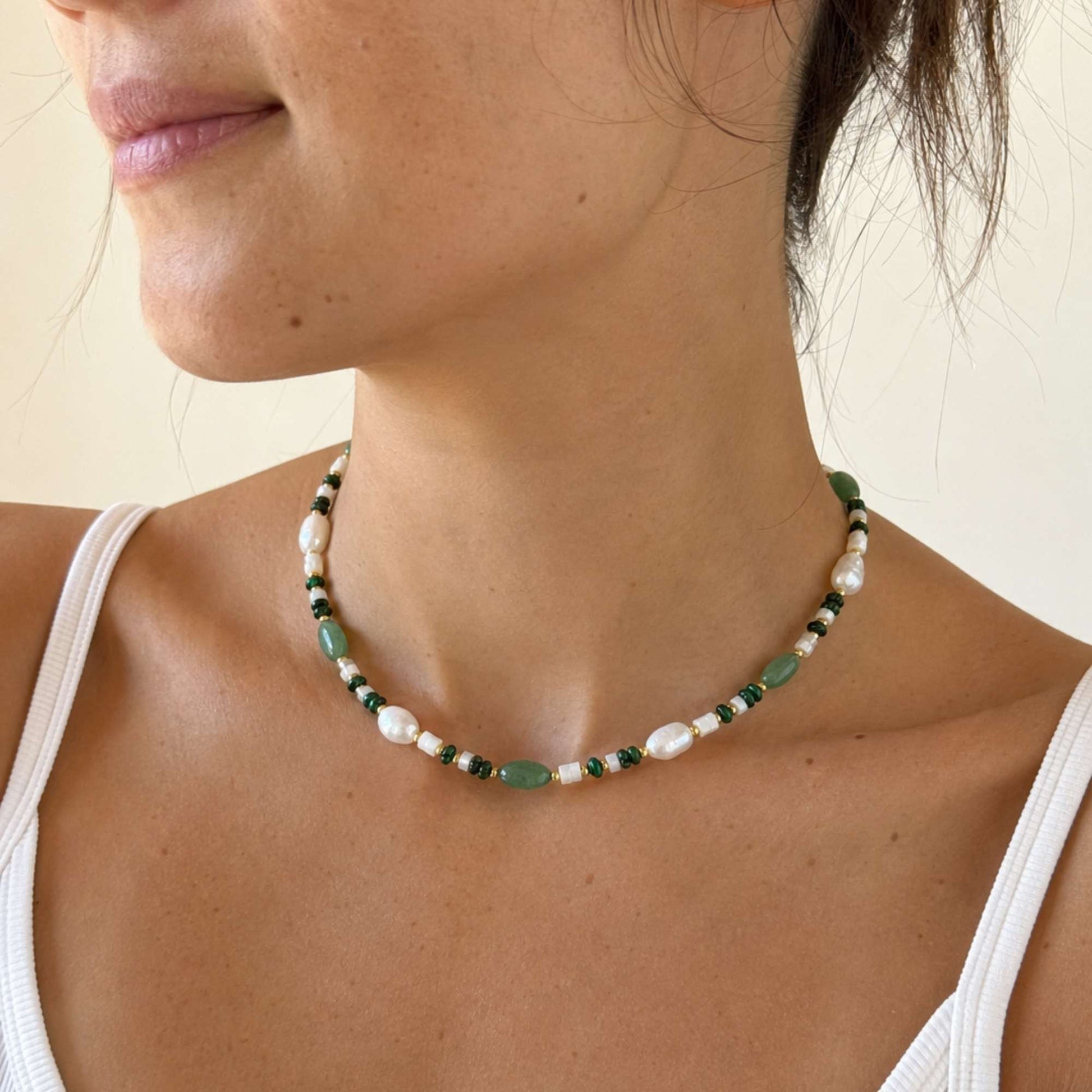 Model wearing a green stone and freshwater pearl necklace with warm gold details.