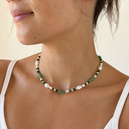 Model wearing a green stone and freshwater pearl necklace with warm gold details.
