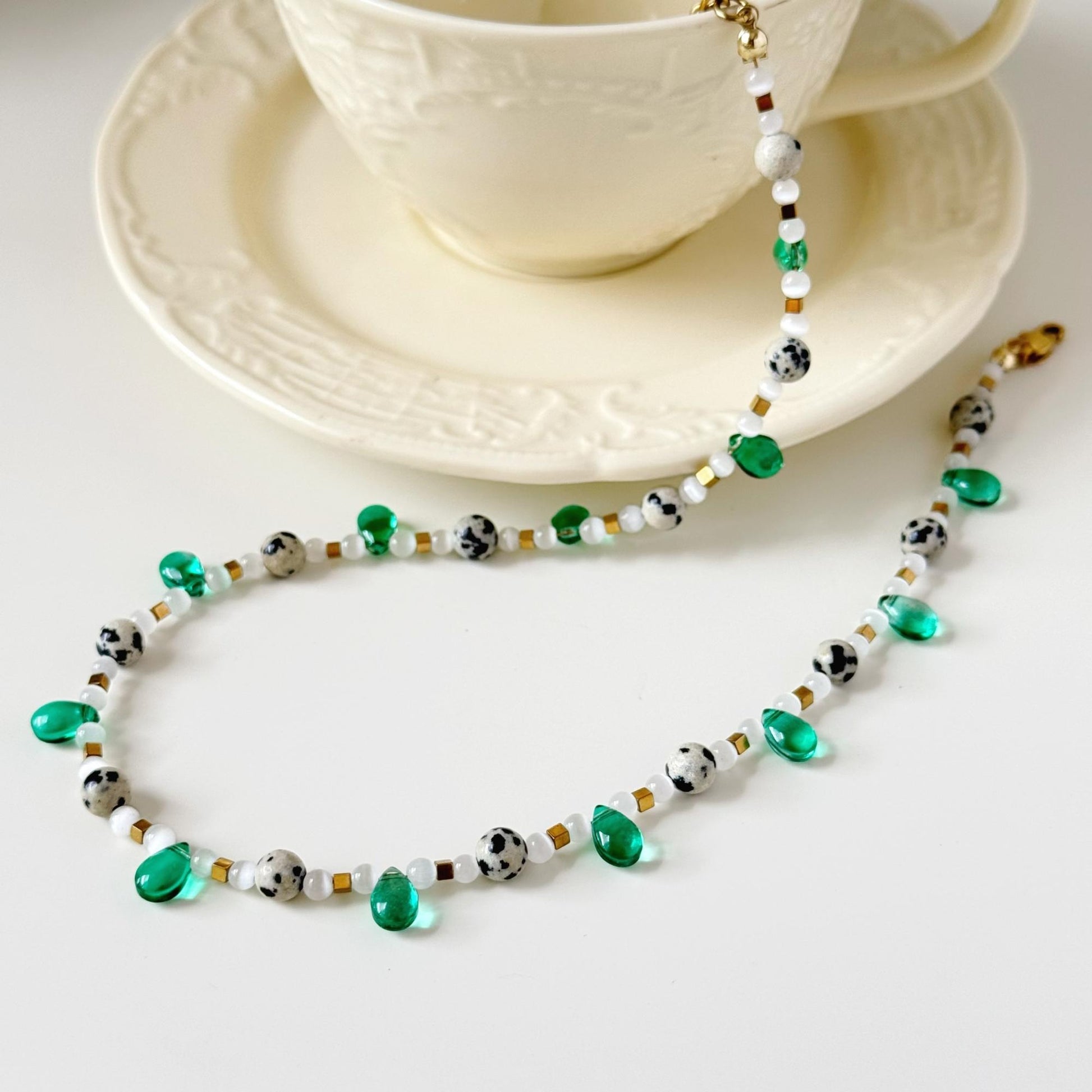 Close-up of green drop beads, speckled stones, white beads, and gold-tone spacers.