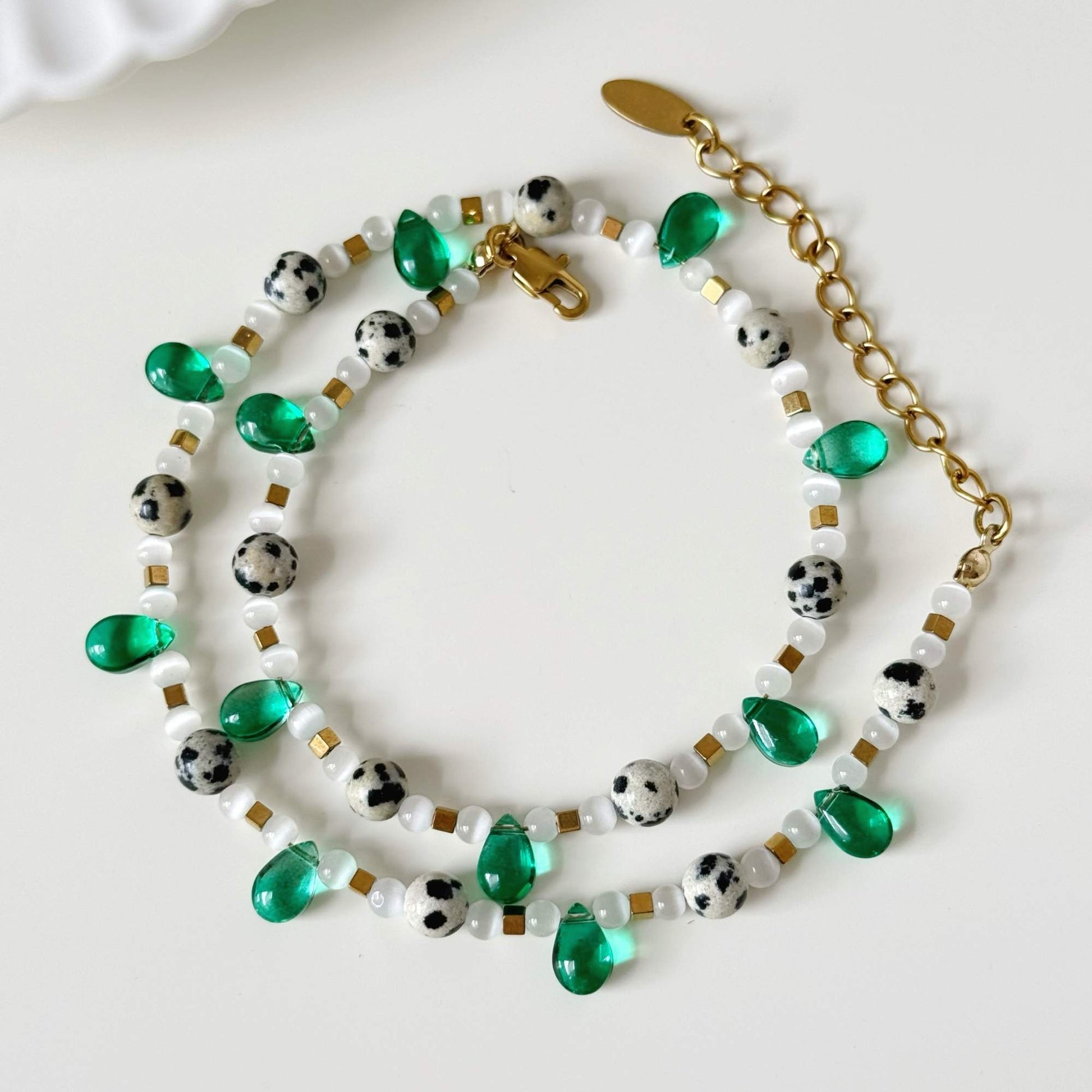 Green and white beaded necklace arranged beside a cream teacup in soft natural light.