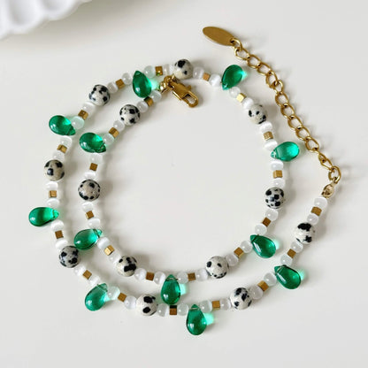 Green and white beaded necklace arranged beside a cream teacup in soft natural light.