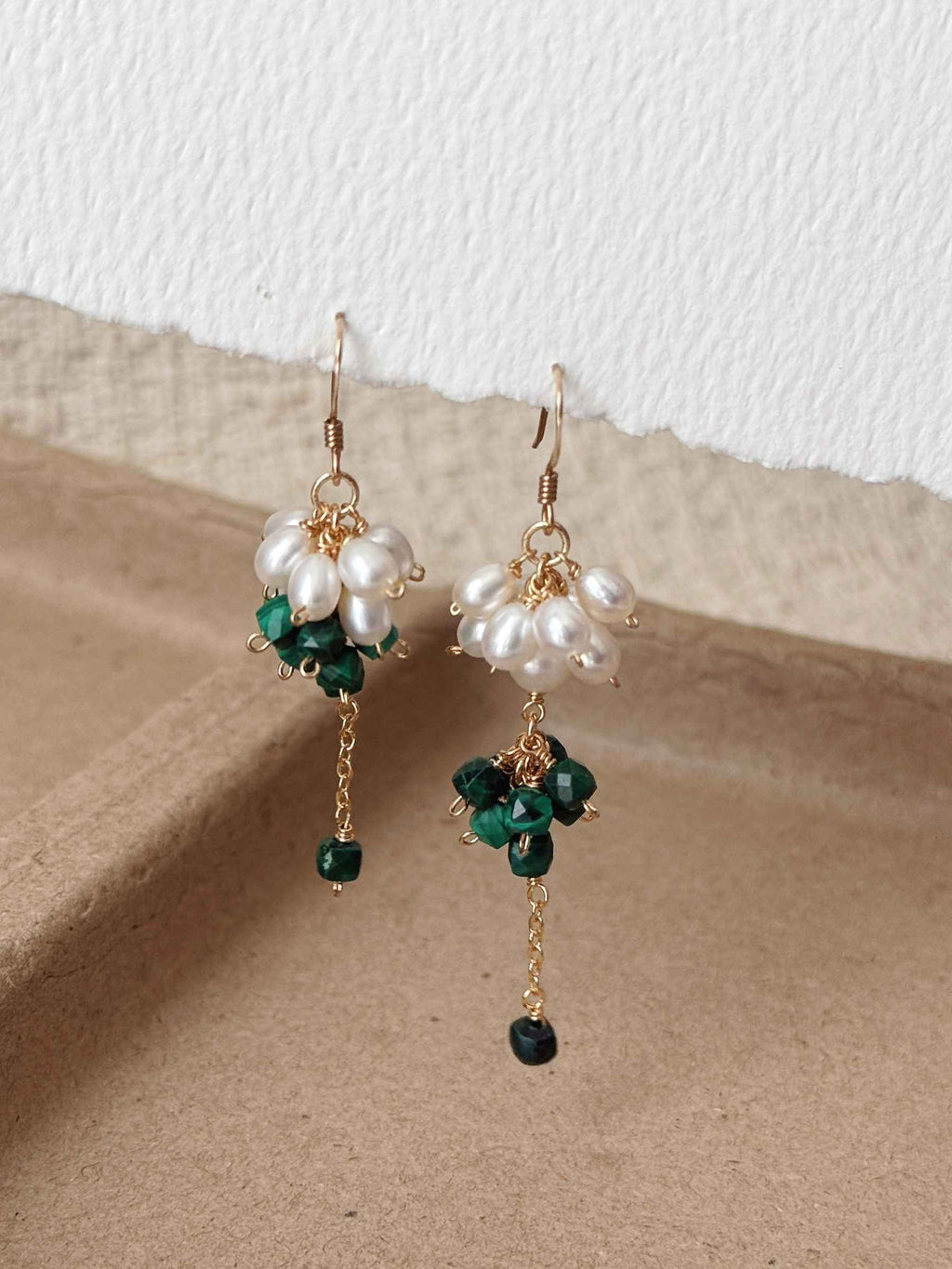 Pair of Grove malachite and freshwater pearl earrings displayed on warm neutral paper with delicate chain drops.