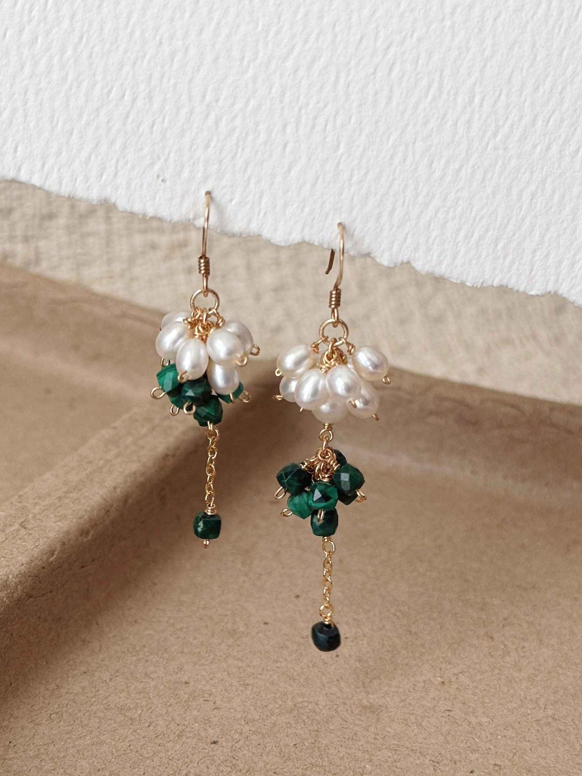 Pair of Grove malachite and freshwater pearl earrings displayed on warm neutral paper with delicate chain drops.