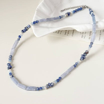 Soft blue natural stone necklace with freshwater pearls styled on a light surface.