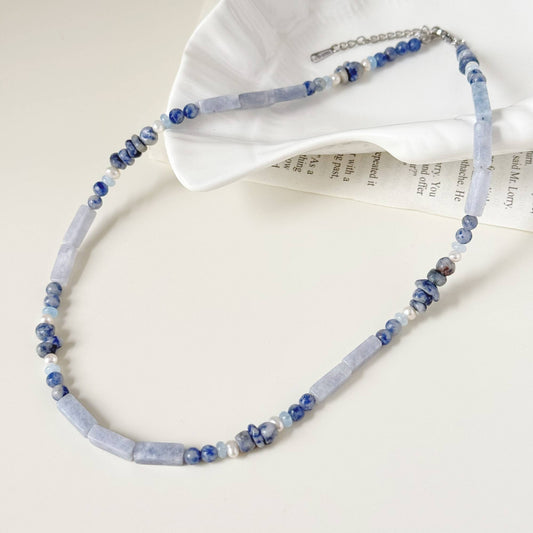 Soft blue natural stone necklace with freshwater pearls styled on a light surface.