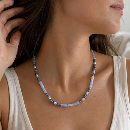 Model wearing a soft blue-gray agate and pearl necklace with a white top in natural light.