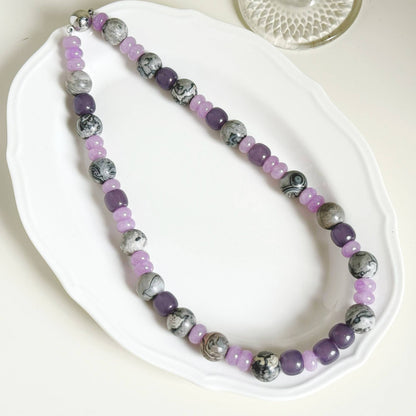 Purple and gray stone necklace arranged on a white dish and natural linen.