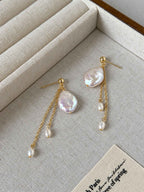 Lilt baroque pearl earrings arranged on a beige linen jewelry tray with delicate gold chain drops.