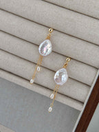 Close view of Lilt baroque pearl earrings on a linen jewelry tray, showing iridescent pearls and fine gold chains.